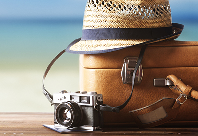 Foto de cmera fotogrfica, mala e chapu com uma praia ao fundo